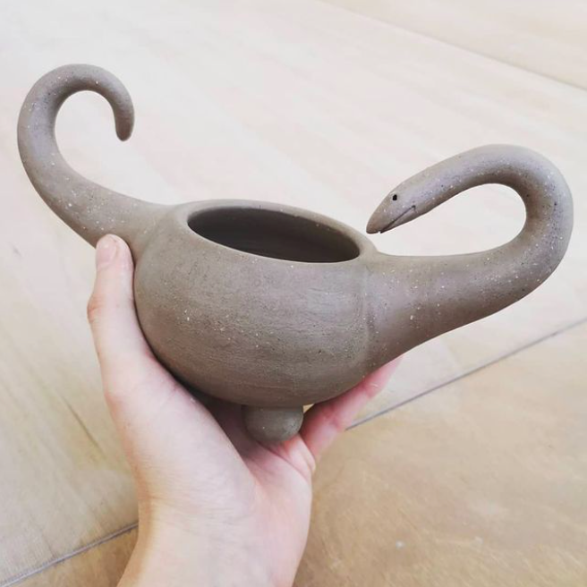 holding a work in progress ceramic dinosaur